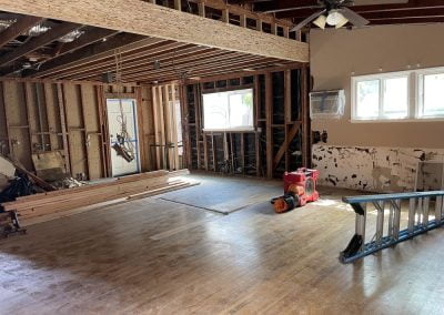 A room undergoing renovation with exposed wooden beams, construction materials, and tools scattered around, reminiscent of a California garage conversion in progress.