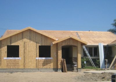 A house under construction in California features unfinished wood framing and roofing, with a ladder leaning against the side, hinting at future kitchen remodeling efforts.