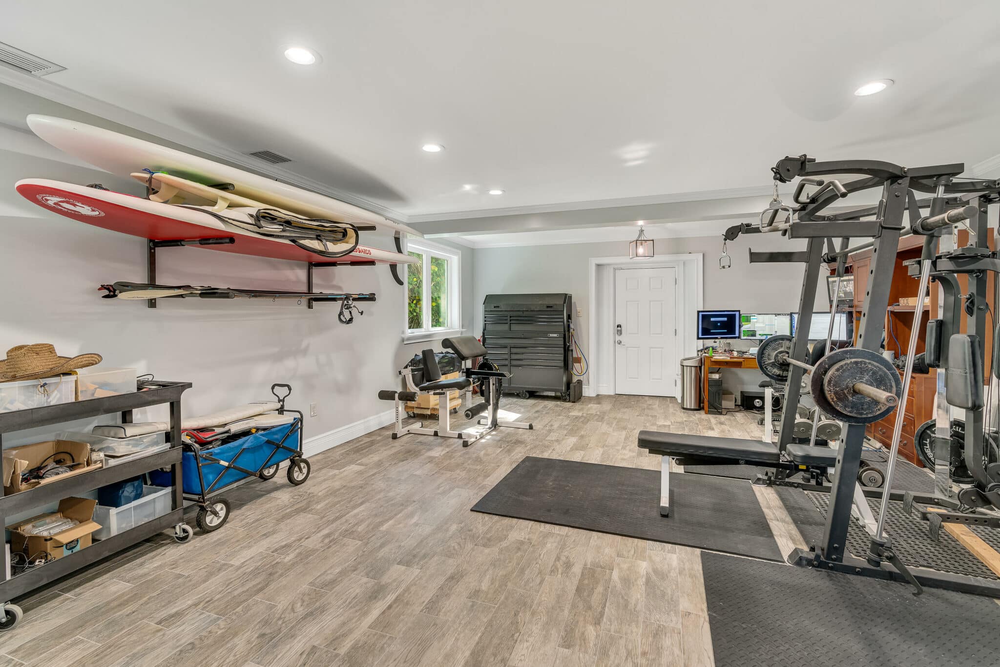 garage conversion ideas Home gym with exercise equipment, surfboards on a wall rack, and organized storage in a bright, spacious room.