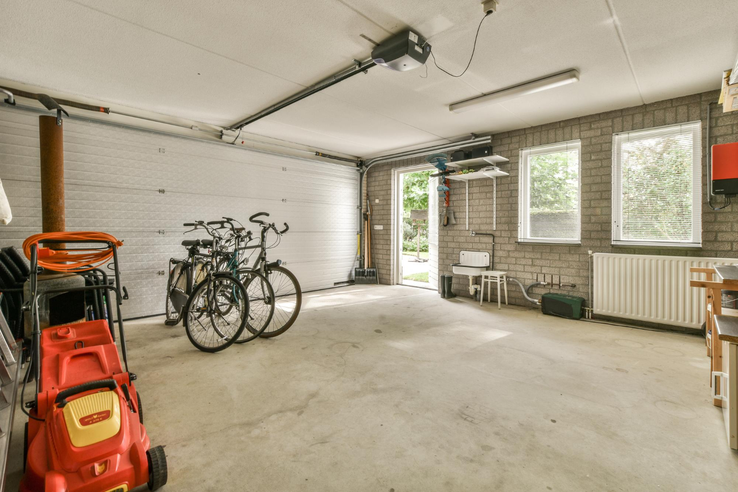 Spacious garage with bicycles, lawnmower, and open door letting in natural light through windows.